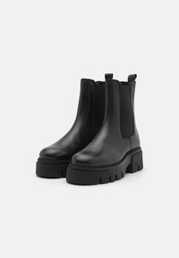 Botas Chelsea de cuero negro con una suela gruesa negra, que cuentan con paneles elásticos laterales y tiradores para facilitar el calzado. Textura suave.