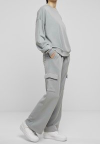 Sudadera gris claro de gran tamaño con hombros caídos, combinada con pantalones cargo a juego que tienen bolsillos laterales y un ajuste relajado. Zapatillas blancas.