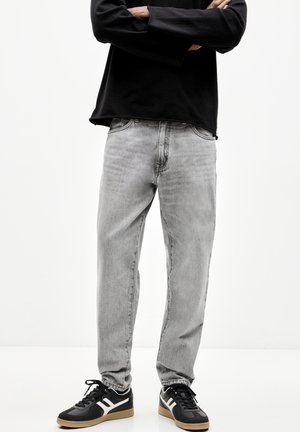 Jeans grigi a gamba dritta con un lavaggio sbiadito, design a cinque tasche e cuciture sottili, abbinati a sneaker nere con dettagli bianchi.