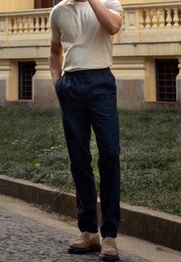 Marina byxor med elastisk midja och sidofickor, i kombination med en ljusgrå t-shirt och beige loafers. Marken är av kullersten med gräs.