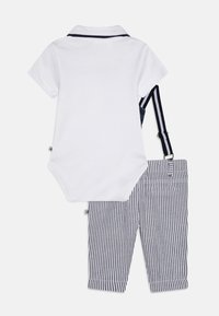 Άσπρο polo bodysuit με ναυτικό trim συνδυασμένο με παντελόνια μπλε και λευκές ρίγες με τιράντες και γυριστό στρίφωμα.