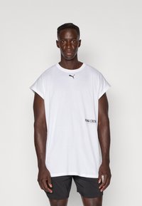 T-shirt en coton blanc à manches courtes avec un col rond et un petit logo Puma noir sur la poitrine. Présente le texte "PIMA CREW" sur le côté.