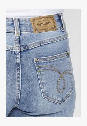 Svijetloplave traperice s oznakom od smeđe kože, stražnjim džepom s ukrasnim šavovima i laganom teksturom.