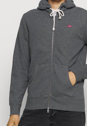 Persoon draagt een donkergrijze hoodie met ritssluiting, voorzakken, witte trekkoorden en een rood Levi's-logo op de linkerborst.