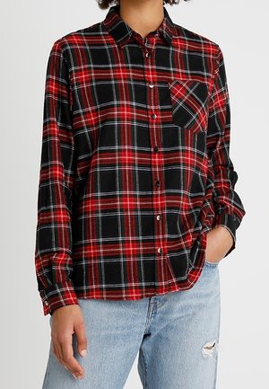Camicia in flanella a quadri rossi e neri con maniche lunghe, chiusura con bottoni e una tasca sul petto. Texture morbida e vestibilità comoda.