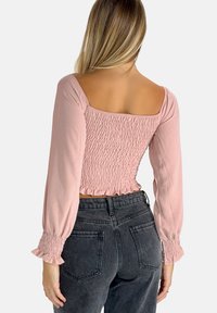 Top corto rosa chiaro con schiena arricciata, maniche larghe e polsini a volants, abbinato a jeans neri a vita alta.