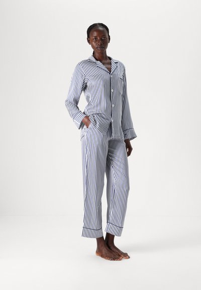 Dryžuotas medvilnės pižamos komplektas mėlynos ir baltos spalvų, su mygtukais užsegama marškinėliais ilgomis rankovėmis ir atitinkamomis kelnėmis su manžetėmis ir šoninėmis kišenėmis.