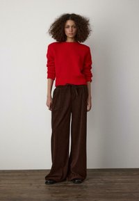 Czerwony sweter dziany z okrągłym dekoltem i długimi rękawami, zestawiony z szerokimi brązowymi spodniami sztruksowymi z troczkiem w talii. Czarne buty.