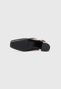 Brown leather shoe sole with a squared shape, textured black rubber grip, and decorative hardware elements on the upper side.