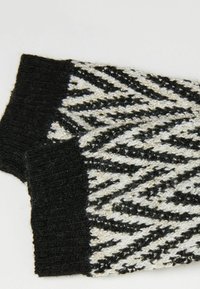 Des manches tricotées en noir et blanc présentent un motif en zigzag avec des fils métalliques. La texture est douce et extensible, offrant une chaleur adéquate.