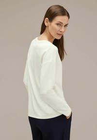 Maglietta bianca a maniche lunghe in tessuto morbido con vestibilità rilassata. Collo rotondo e spalle scese, abbinata a pantaloni a coste blu navy.