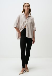 Camicia oversize rosa chiaro con maniche corte, chiusura a bottoni, abbinata a leggings neri e scarpe con tacco nudo. Texture semplici e morbide.