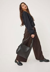 Schwarze Lederhandtasche mit strukturiertem Design, ausgestattet mit einem breiten Träger und goldfarbigen Akzenten. Trägt man zu einem schwarzen Oberteil und braunen Hosen.