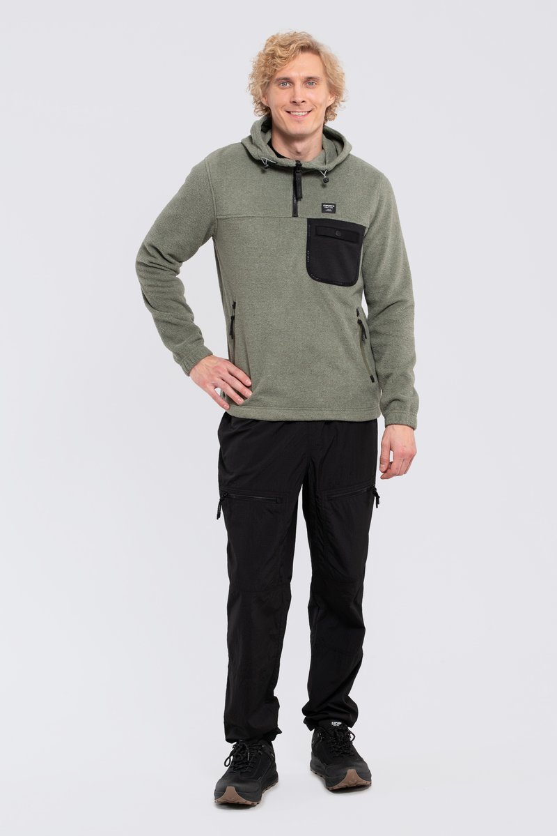 Pullover in pile verde con cappuccio, tasca sul petto nera con zip e tasche laterali. Pantaloni cargo neri con tasche con zip, abbinati a scarpe nere.