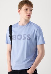 T-shirt en coton bleu clair avec un col rond et des manches courtes, affichant un grand imprimé en gras "BOSS" en gris sur la poitrine.