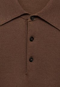 Braun gestricktes Polohemd mit kragenförmigem Ausschnitt, vier schwarzen Knöpfen und strukturiertem Stoff. Nahaufnahme zeigt Details und Nähte.