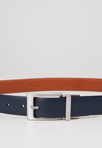 Cinturón de cuero navy con un acabado suave, que presenta una hebilla de metal plateada y una capa interior en tono marrón claro contrastante. Incluye agujeros para ajuste.