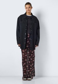 Svart denim oversized skjorta, kortärmad svart topp och svart blommig genomskinlig maxikjol med röda och gröna detaljer. Beiga skor.