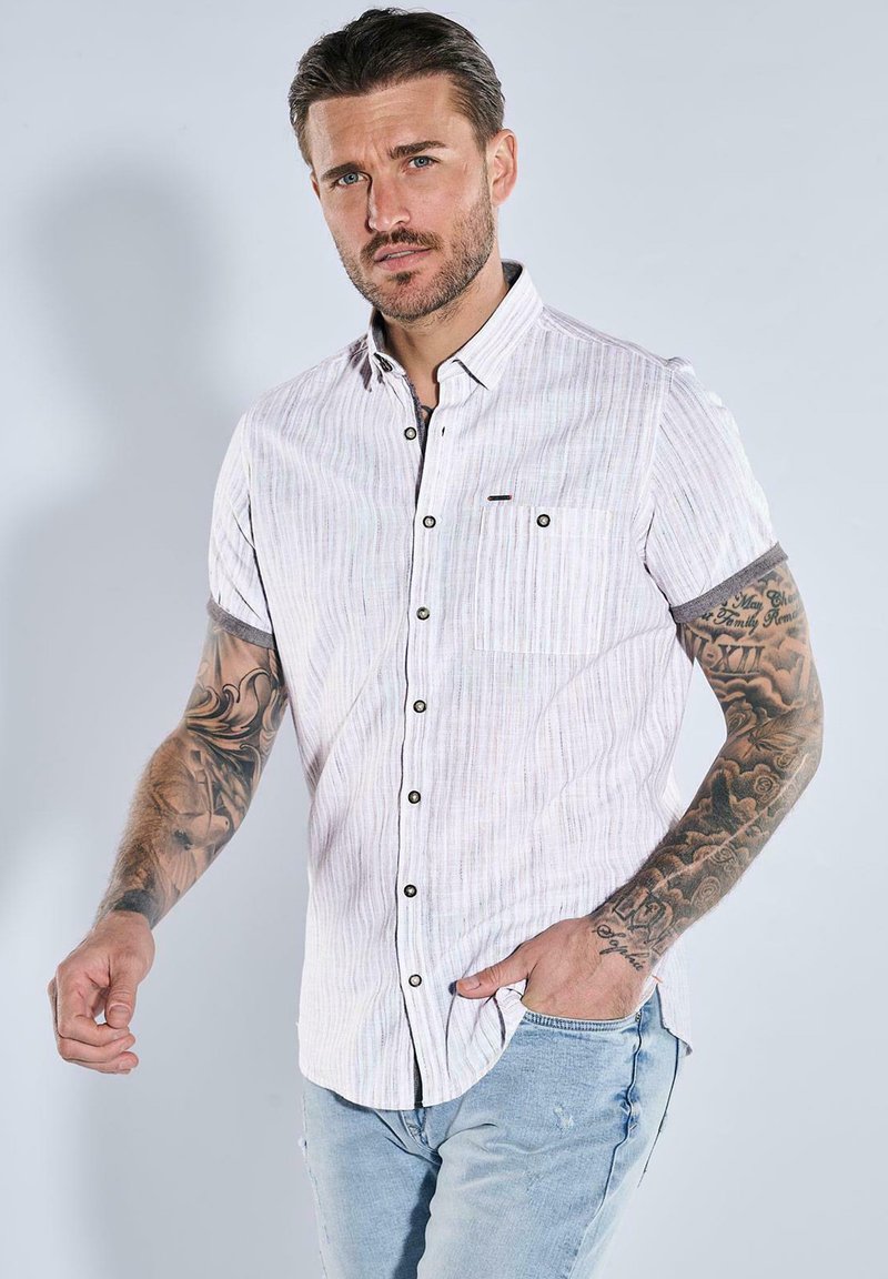 Hemd mit kurzen Ärmeln in Lichtrosa mit feinen Streifen, ausgestattet mit einer durchgehenden Knopfleiste, Brusttasche und dunklen Knöpfen; eine Jeans aus Denim ergänzt den Look.