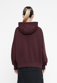 Sweatshirt burdeos com um bolso frontal, ajuste oversized e capuz com cordão. Textura suave e punhos canelados nas mangas e na parte inferior.
