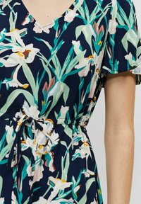 Blumenmuster-Kleid aus dunkelblauem Stoff mit V-Ausschnitt, kurzen Ärmeln und einem bindbaren Taillenband, verziert mit einem Muster aus weißen und pinken Blumen sowie grünen Blättern.