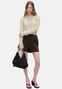 Lichtbeige opengehaakte lange mouw top, donkergroene shorts, zwarte geweven tas met knoopdetail en zwarte wedge sandalen.