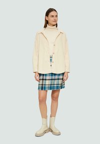 Chemise jacke crème à boutons sur un col roulé blanc, associée à une jupe à carreaux bleus. Bottines beiges à la cheville avec une semelle épaisse.