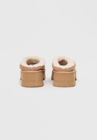 Brown clogs with a plush sheepskin lining, open backs, and thick platform soles. Textured exterior with prominent seams and soft edges.