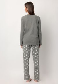Top de manga larga gris combinado con pantalones de pijama grises que presentan un patrón gráfico repetido de calaveras. Tejido suave con un corte holgado.