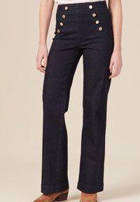 Pantalons en denim foncé taille haute avec cinq boutons dorés décoratifs sur le devant et une coupe droite. Fini en tissu classique et résistant.