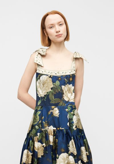Φόρεμα με λουλουδάτο σχέδιο σε μπλε βάση, με λευκά τριαντάφυλλα και πράσινα φύλλα. Τετράγωνη γραμμή στο λαιμό, ιμάντες ώμων με δέσιμο και πολλαπλές στρώσεις στη φούστα.