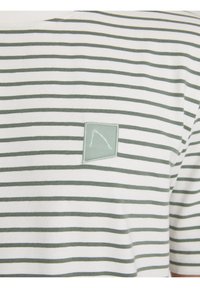 T-shirt a righe realizzata in un morbido tessuto con strisce orizzontali verdi e bianche, caratterizzata da una toppa quadrata con un design contornato sul petto.