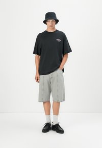 Svart oversized t-skjorte med broderi på forsiden, kombinert med grå denimshorts og svarte snørestøvler. Tilbehøret inkluderer en svart bøttehatt.