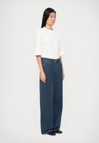 Hvit topp med korte ermer parret med høyt liv og vide, mørk denim-bukser. Glatt stoffoverflate; enkelt design med minimal pynt.