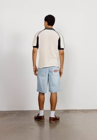 Kortermet strikket jersey i beige med svarte detaljer; kombinert med lyseblå denimshorts med rød broderi på baklommen.