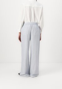 Pantalones de pierna ancha de color azul claro con cintura elástica y dos bolsillos traseros, combinados con una camisa blanca de manga larga y cuello.