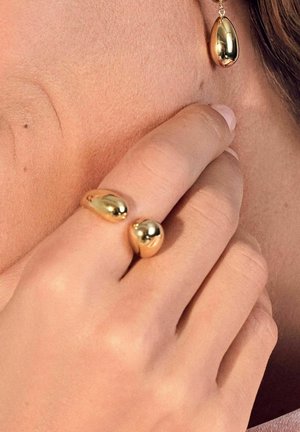 Gold-tone jewelry includes a teardrop earring and a double-bubble ring, both featuring a smooth, reflective finish and rounded shapes.