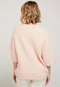 Sweater surdimensionné rose clair en matériau doux avec des manches courtes et un ourlet arrondi. Présente une coupe décontractée et un design simple.