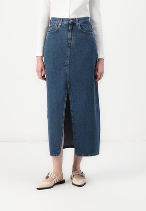 Denim midi skirt with a front slit, high waist, five pockets, and subtle stitching details. Worn with light beige flat shoes.