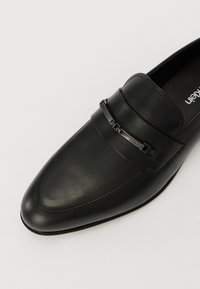 Loafers din piele neagră cu un design elegant, vârf ascuțit și un accent decorativ din curea metallică. Textură netedă cu detalii de cusătură subtile.