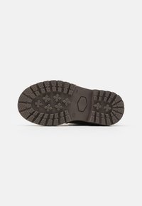 Semelle en caoutchouc noir avec un motif de semelle robuste et des crampons multidirectionnels pour une adhérence optimale. Marque identifiable gravée sur le côté.