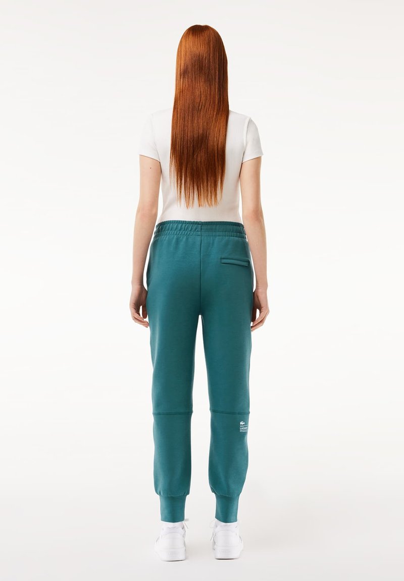 Turkusowe dresowe spodnie wykonane z miękkiego materiału, posiadające sznurek w pasie, elastyczne ściągacze oraz naszywkę z logo na dolnej części nogawki.