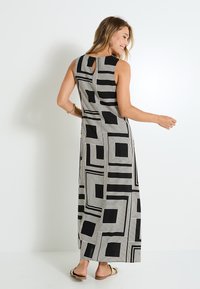 Robe maxi noir et blanc présentant un motif géométrique de carrés, détail en forme de clé à l'arrière, et design sans manches. Tissu doux et fluide.