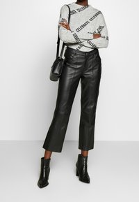 Svarta lädercroppade byxor med en slät yta, i kombination med en grå tröja med svart text. Ytterligare svarta accessoarer ingår.