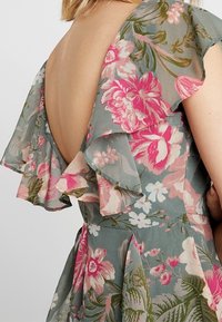 Tylny widok sukienki w kwiaty z dużymi różowymi kwiatami, falbankowymi rękawami i głębokim dekoltem w kształcie litery V.