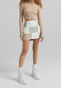 Háčkovaný top s dlouhými rukávy, zkombinovaný s patchworkovou mini suknią v zelené, béžové a bílé barvě. Chunky bílé kotníkové boty dotvářejí celý vzhled.