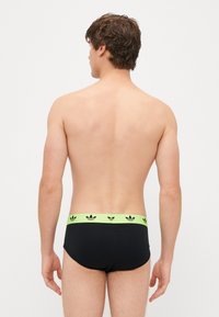 Fekete, boxer stílusú alsónemű neon zöld elasztikus derékkal, amelyen ismétlődő logóelemek találhatók. Simább textúra, illeszkedő forma és minimális takarás jellemzi.