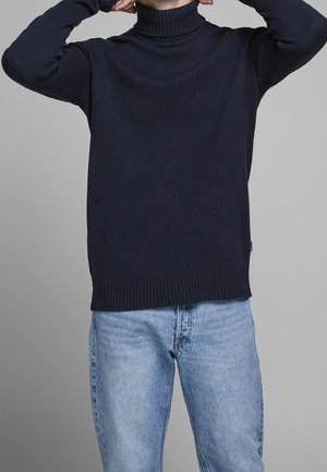 Maglione a collo alto navy in tessuto lavorato a maglia, con polsini e orlo a coste, abbinato a jeans azzurri. Design semplice, senza motivi.