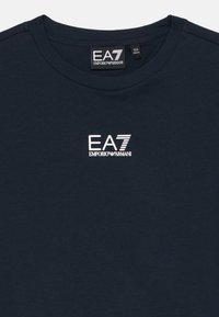 Tamsiai mėlyna medvilninė marškinėlė su apvaliu kaklu, priekyje balta EA7 Emporio Armani logotipas. Lygus tekstūros, paprastas dizainas.