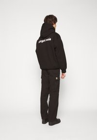 Czarna bluza z kapturem z napisem "rahogari music" na plecach, zestawiona z czarnymi spodniami typu cargo z bocznymi kieszeniami, wszystko o luźnym kroju.